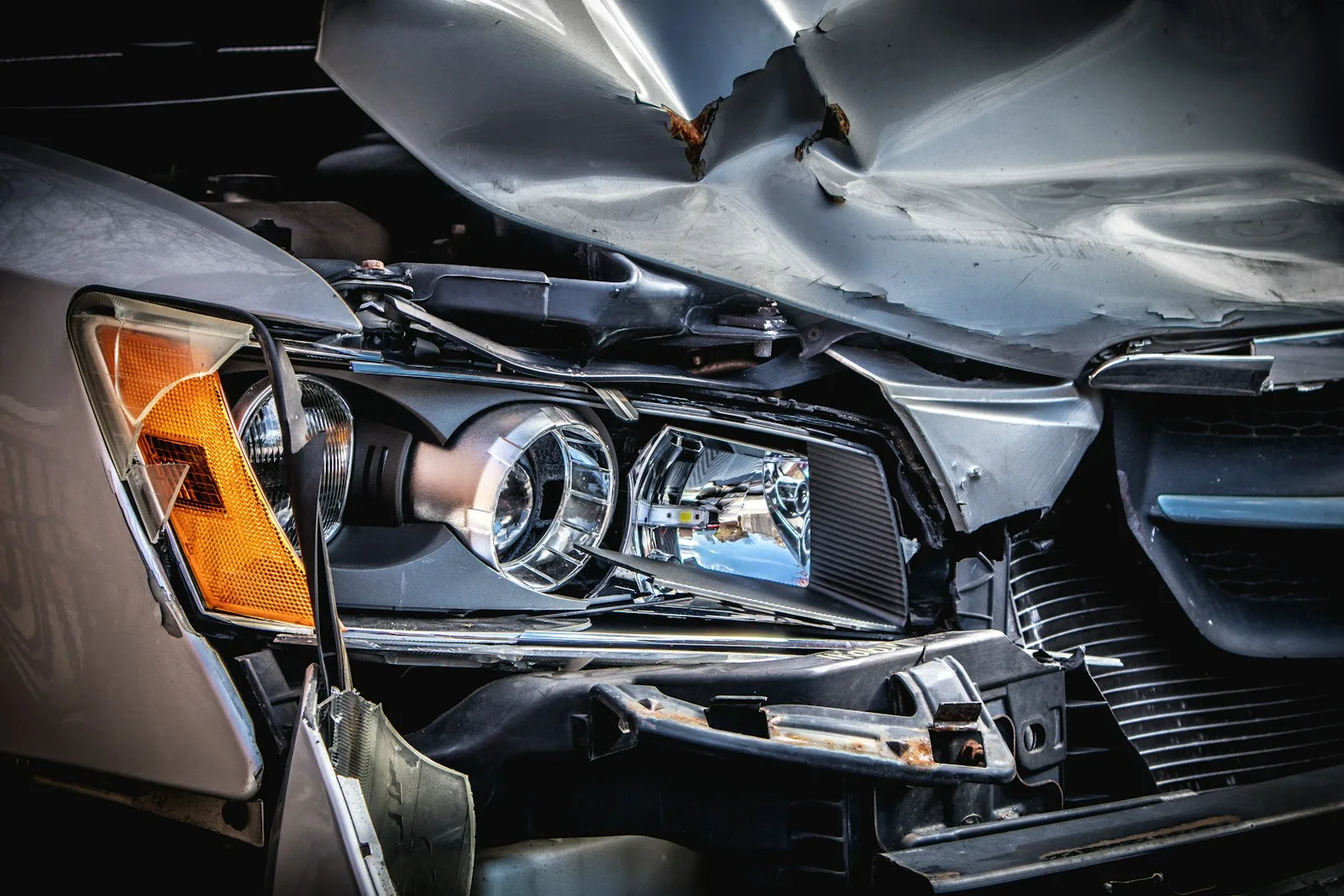 Collision damage to a silver vehicle’s hood and headlight assembly
